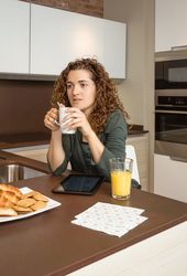 Woman holding coffee over tablet screen at breakfast
