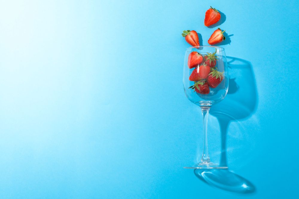 Wine glass with strawberries on color background, space for text. Summer sweet fruits and berries