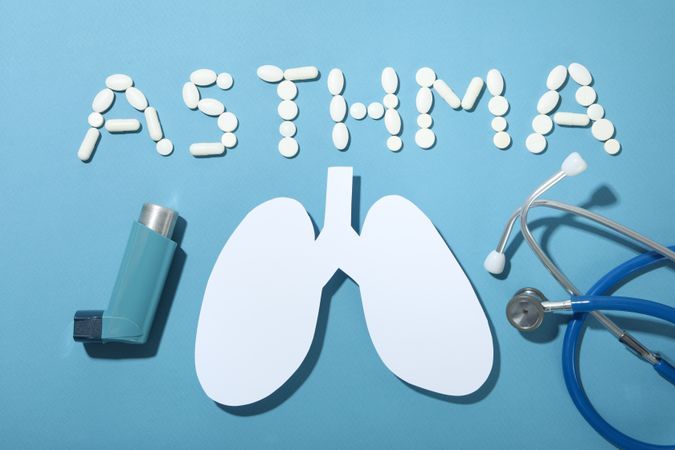 Asthma spelled in pills with lungs, inhaler, and stethoscope