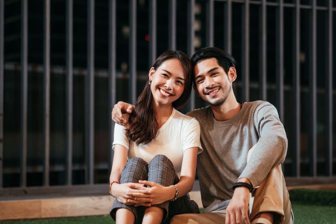 Man embraces woman's shoulder while sitting together outside