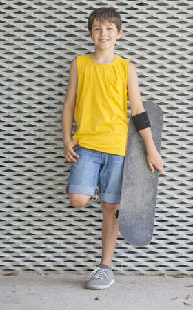 A teenage boy posing with skateboard and smiling against metal wall