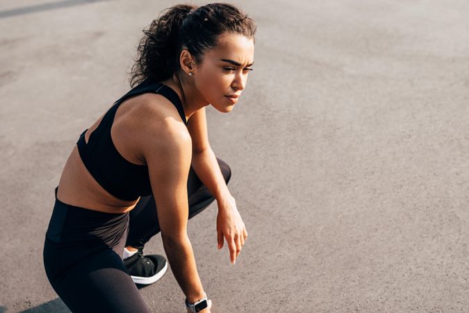 Woman in exercise gear crouching down on concrete