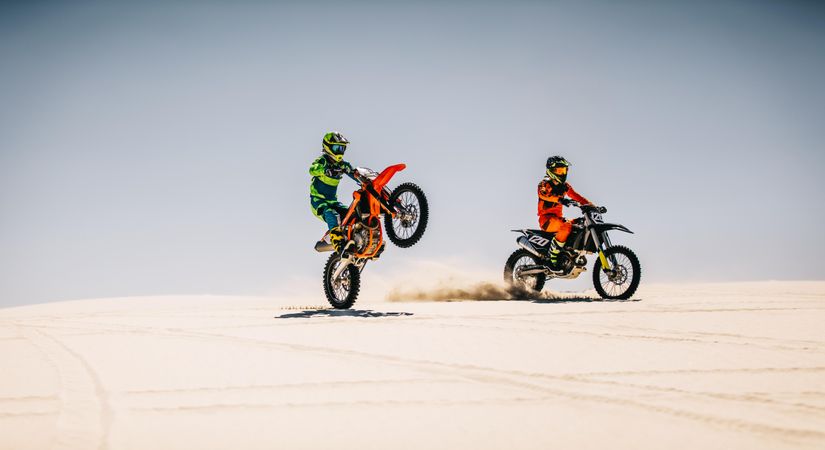 Two motocross riders riding bikes in desert