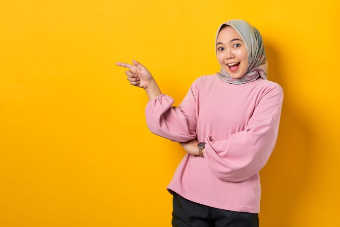Excited Muslim woman in head scarf pointing to her side
