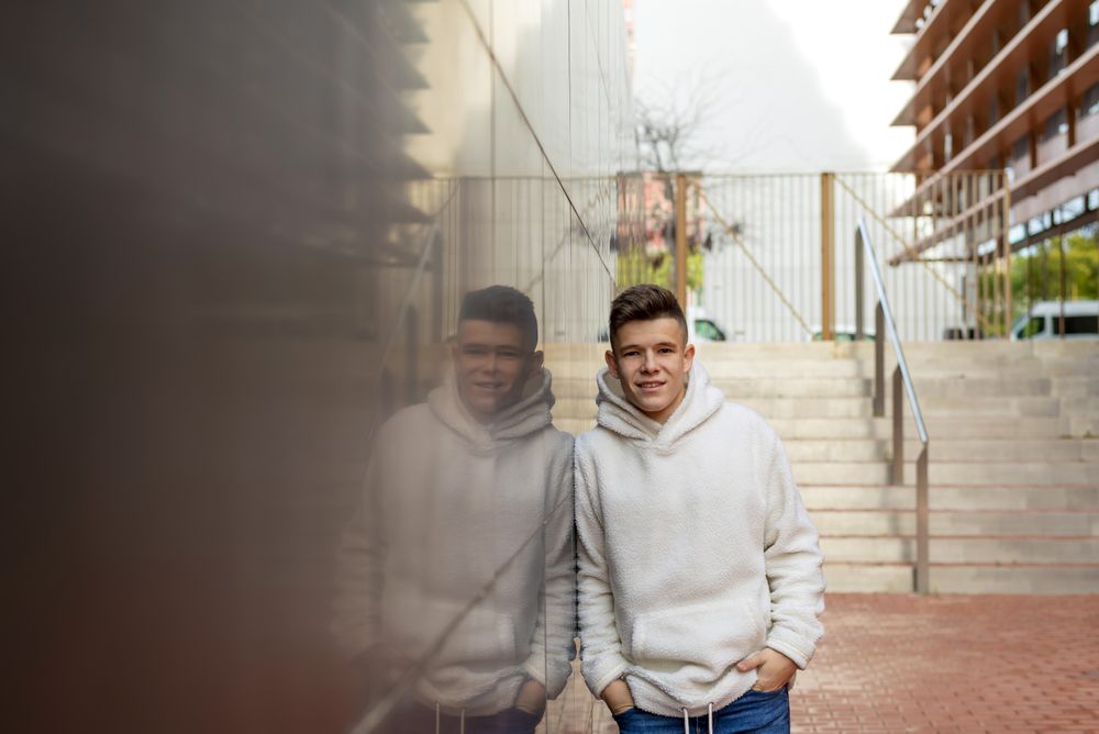 Portrait of young male with hands on pocket leaning on wall outside by staircase