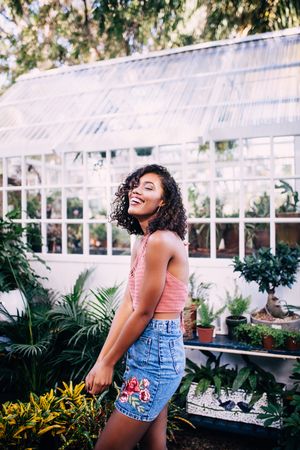Young woman standing in front of a greenhouse smiling in a cheerful manner