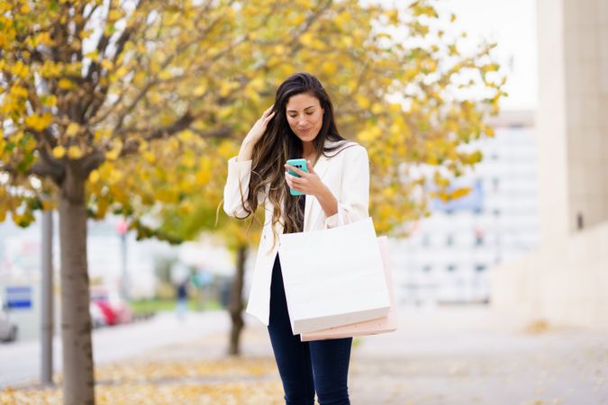 A woman is shopping on a lovely fall day, happily using her smartphone while exploring the city