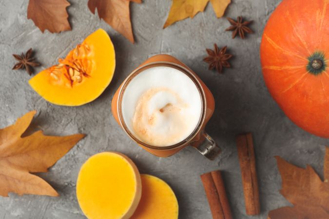 Composition with pumpkin latte, pumpkin, leaves and cinnamon on gray table