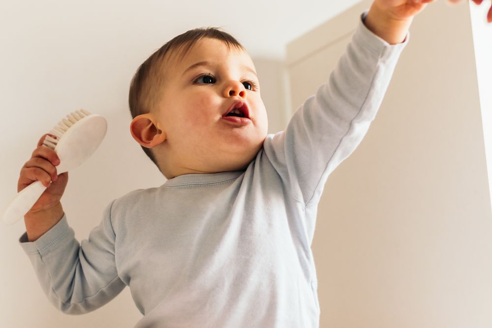 adorable and beautiful baby sitting with a hair brush pointing at something