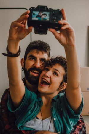 Joyful couple embracing and taking selfie on camera at home