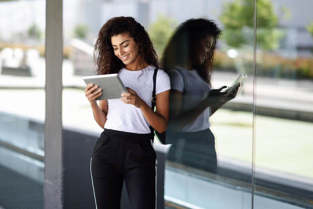 Happy Arab woman using digital tablet in front of office building