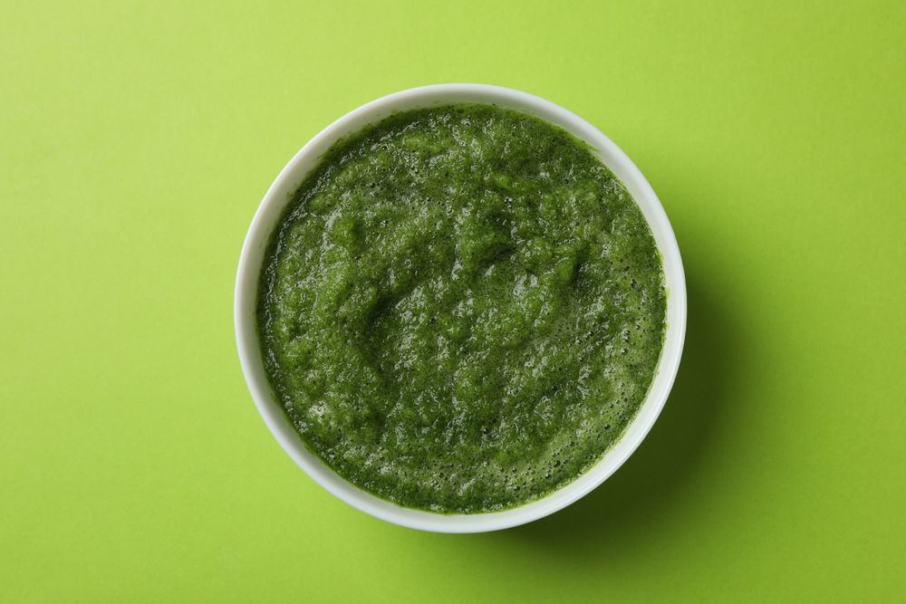 Top view of bowl of broccoli soup on green table