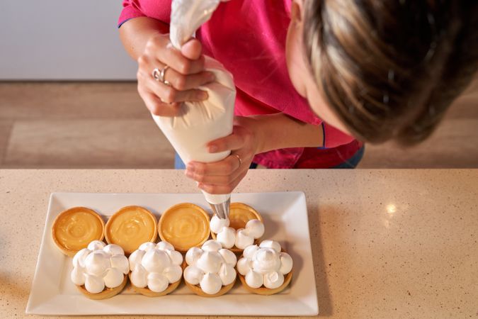 Crop female pastry chef making peaks of cream on tarts
