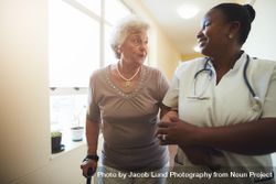Nurse assisting mature female patient while walking in nursing home 5nNEQ5