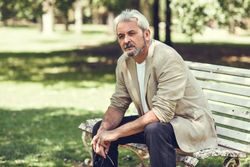 Portrait of a mature man, sitting forward on bench in a park with copy space