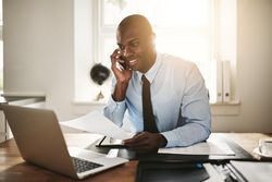 Man in suit and tie smiling on phone while working on his laptop