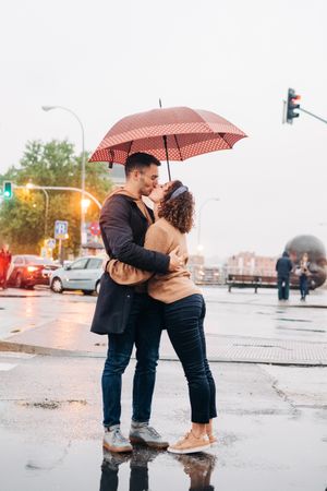 Happy couple with umbrella hugging on wet street