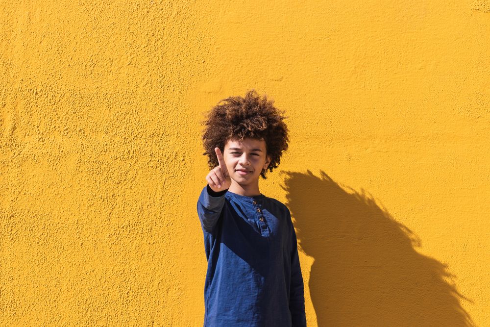Black boy with curly hair pointing at camera