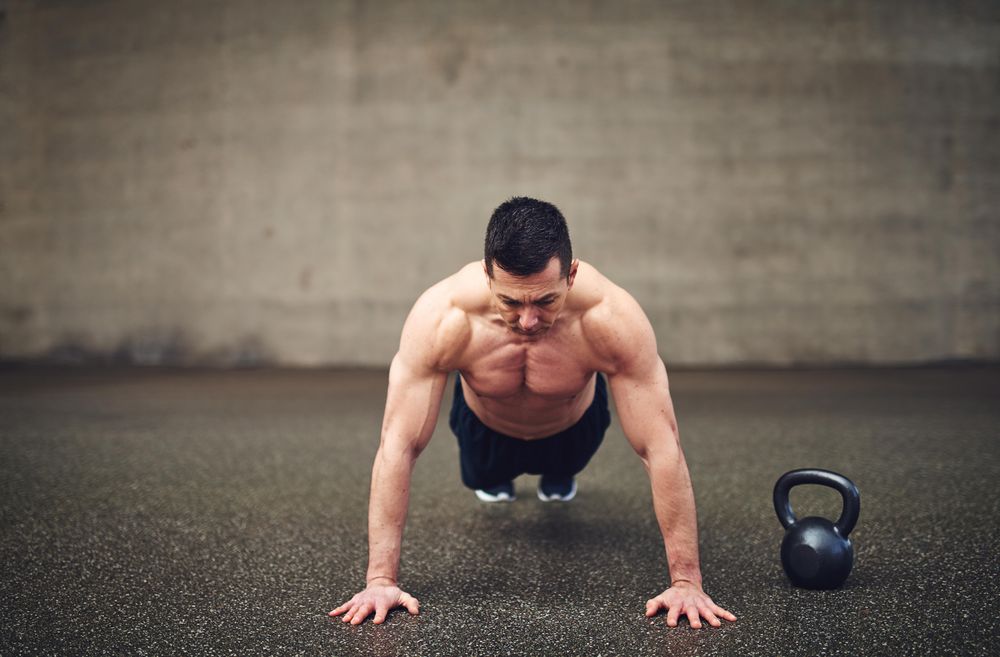 Man doing planks in concrete space next to weight