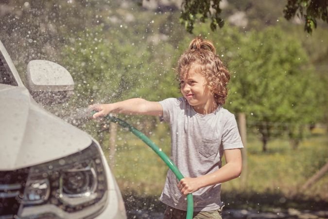 Cheerful boy splashing water on car