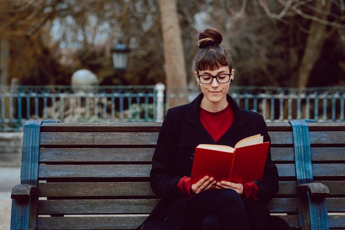 Young woman reading book on bench in park