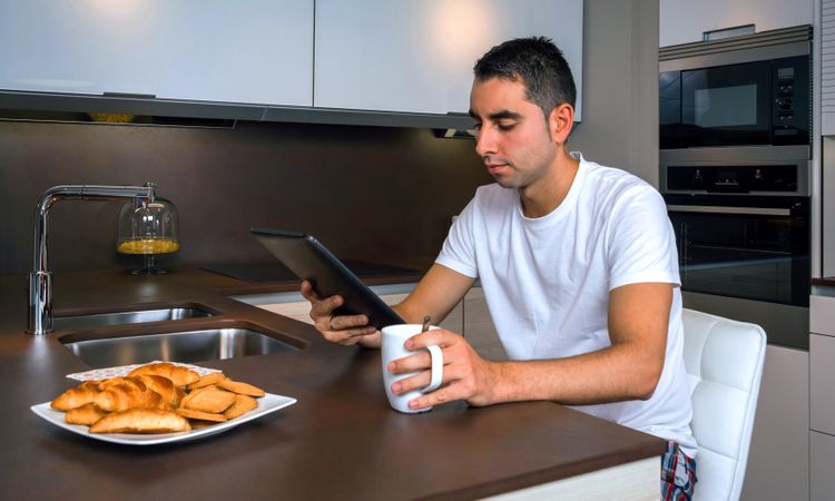 Man reading tablet during breakfast with cup of coffee and pastries