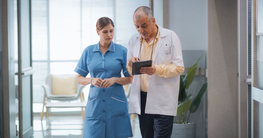 Portrait of Indian Male Doctor and Female Nurse Walking in Hospital Corridor and Talking while Using a Digital Tablet.