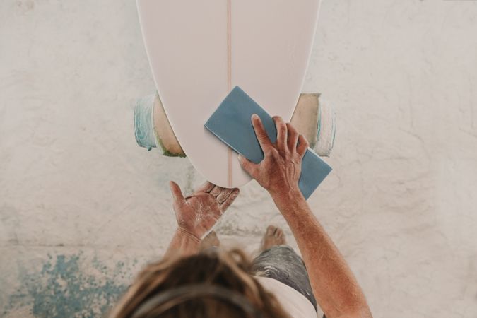 Man in respirator polishing surf board in workshop
