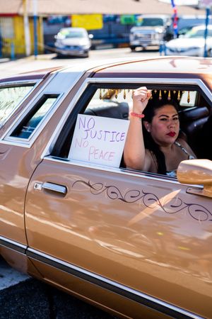 Los Angeles, CA, USA — June 7th, 2020: woman looking out of car window with protest fist in the air