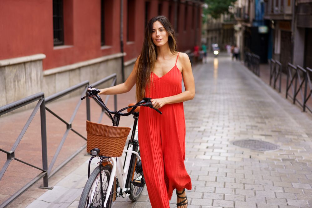 A Stylish Woman Dressed in a Red Dress Walking Gracefully with a ebike through an Urban Setting