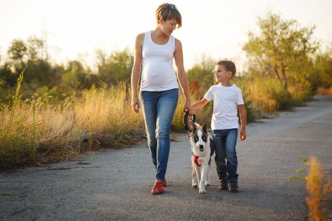 Expecting woman and young boy take their dog for walk on road
