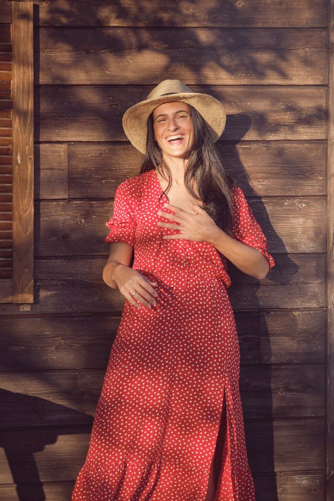 Young cheerful woman in red dress standing near wood wall