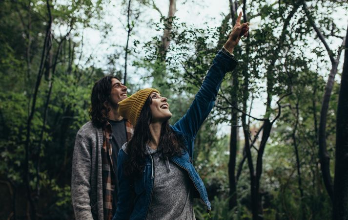 Young couple standing together in forest, with woman pointing up and smiling
