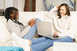 Two women sitting on couch using laptop