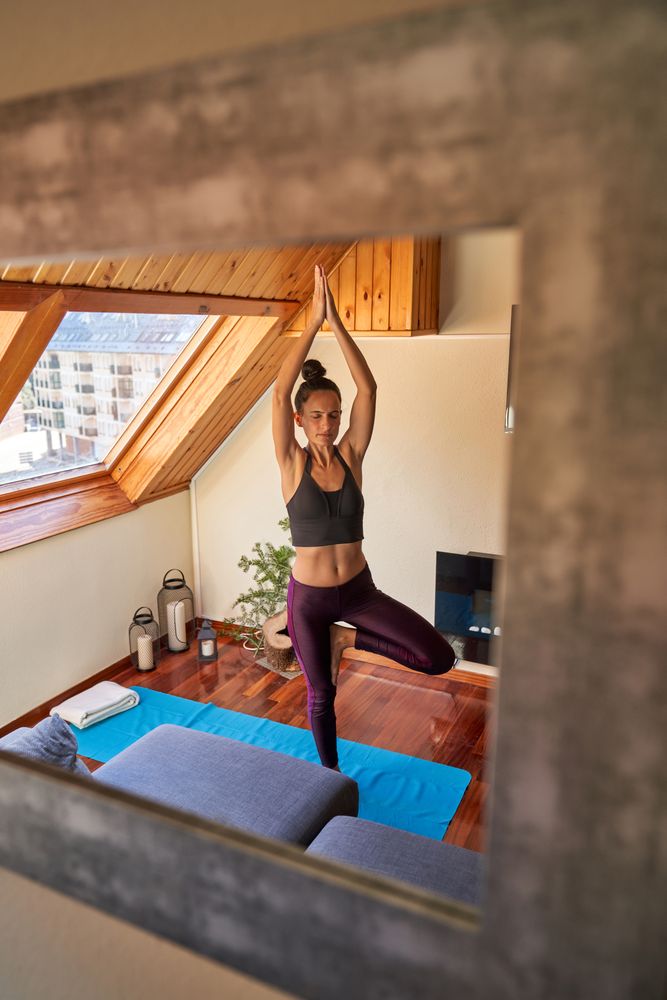 Slim young woman standing in Tree yoga pose on mat