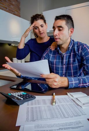 Stressed couple organizing bills together in their kitchen, vertical