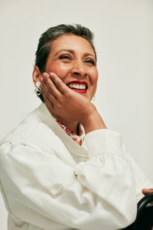 Woman in cream-colored jacket with hand on chin and smiling