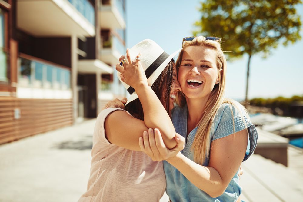 Two female friends laughing and walking along the river on a sunny day