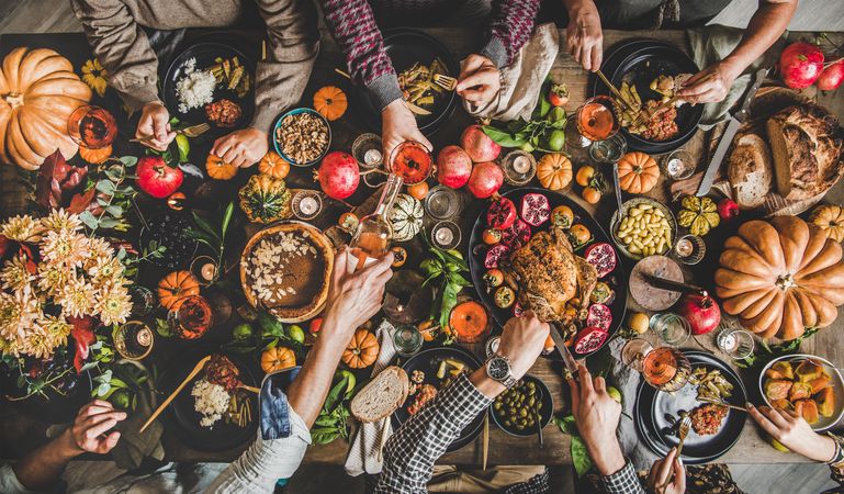 Group of people serving food and pouring wine at festive table with roast chicken, squash and pie