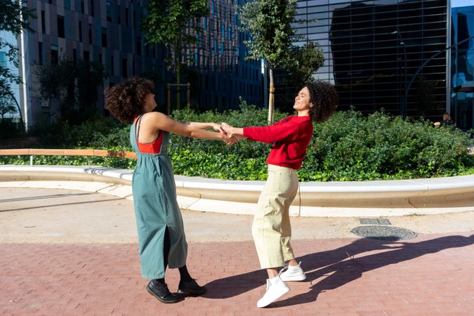 Female friends spinning each other outside on sunny day