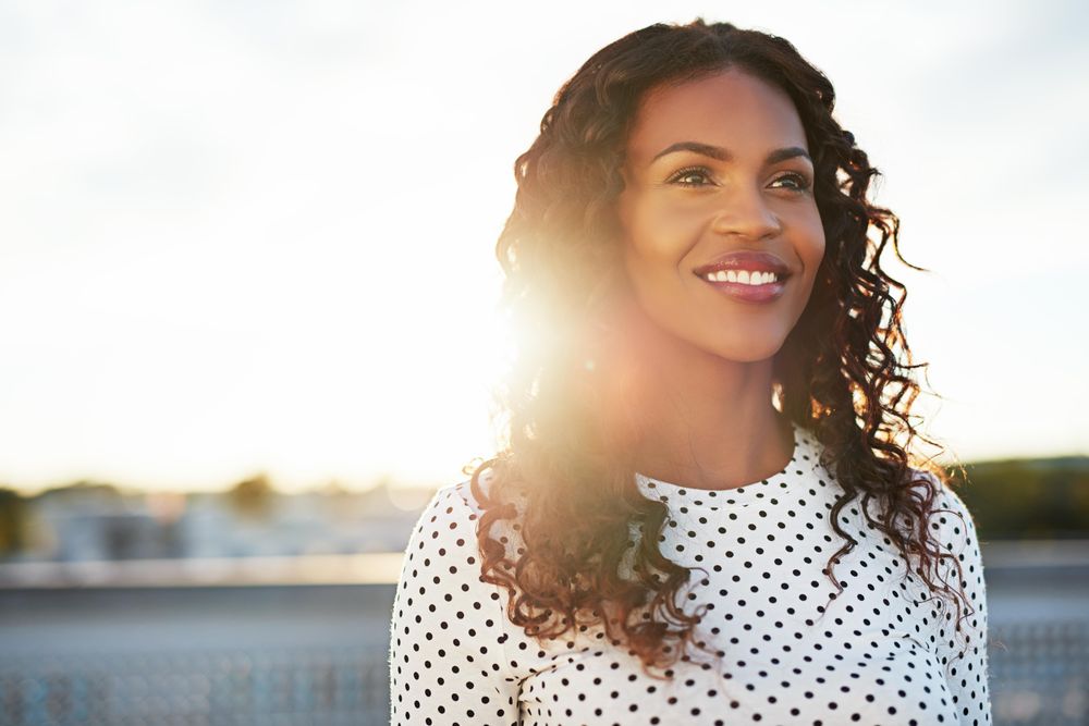 Black woman standing on sunny rooftop smiling into the distance