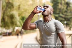Athletic male drinking from a water bottle in an outdoor park 5n2QD5