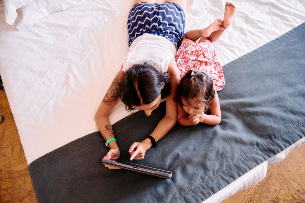 Little girl and her mother using a tablet in a hotel room