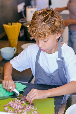 Boy cutting bacon while cooking in kitchen