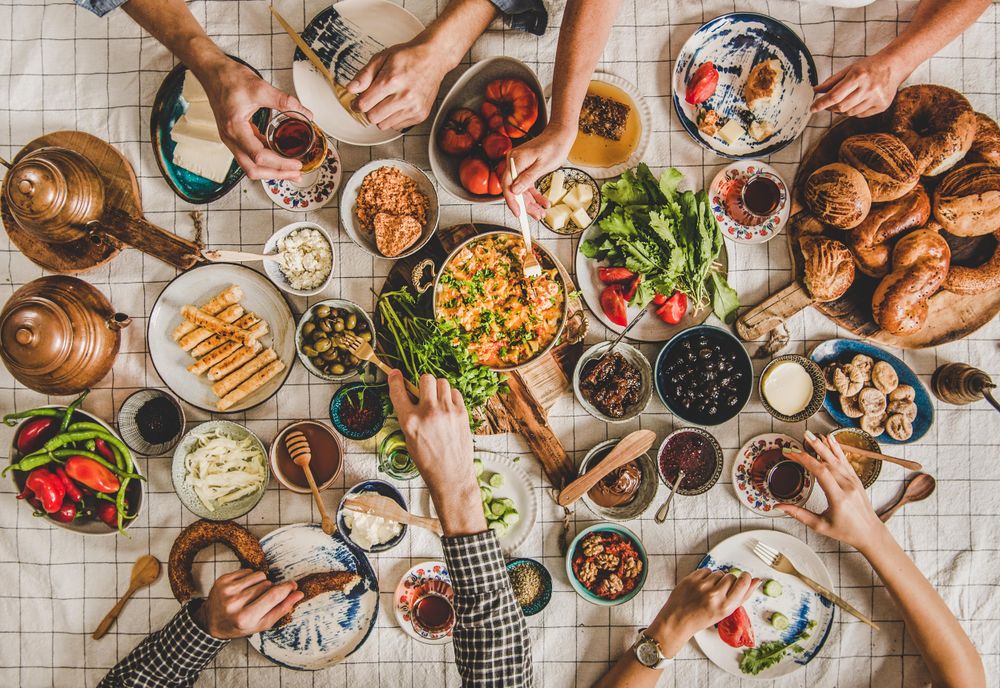 Group of people serving themselves at Turkish style breakfast with eggs, breads, vegetables, tea