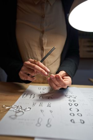 Crop goldsmith working at table under lamp