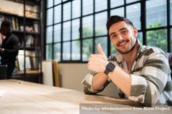 Man in bright office sitting at table giving thumbs up bepop4