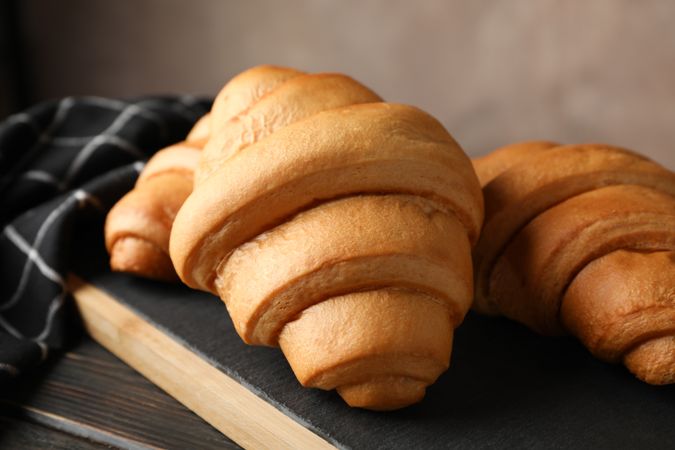 Board with croissants on wooden table with towel, close up