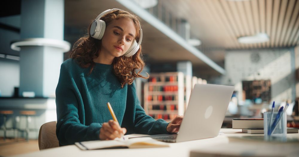Concentrated Young Female Student Engaged in Academic Research With Laptop and Headphones