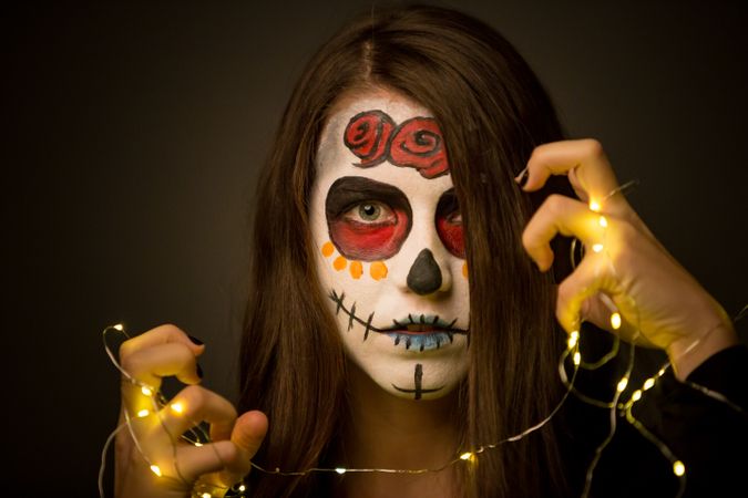 Young woman with creepy face paint holding fairy lights
